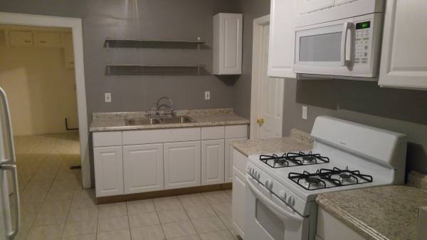 gray kitchen with white cabinets. white stove with microwave above stove. sink with shelves above sink