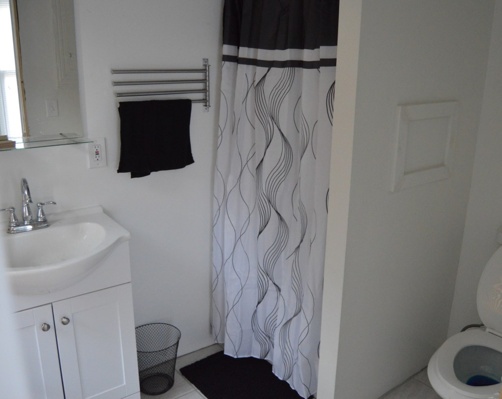 bathroom with white sink and mirror. black shower curtain and black mat with black towl hanging on wall