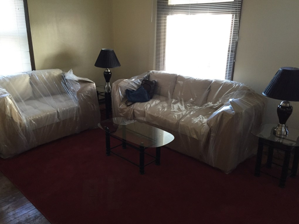 livingroom with cream furniture still in plastic. glass tables and black lamps