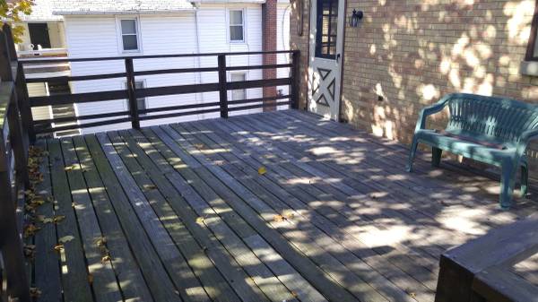 wood porch with door into brick house with green bench