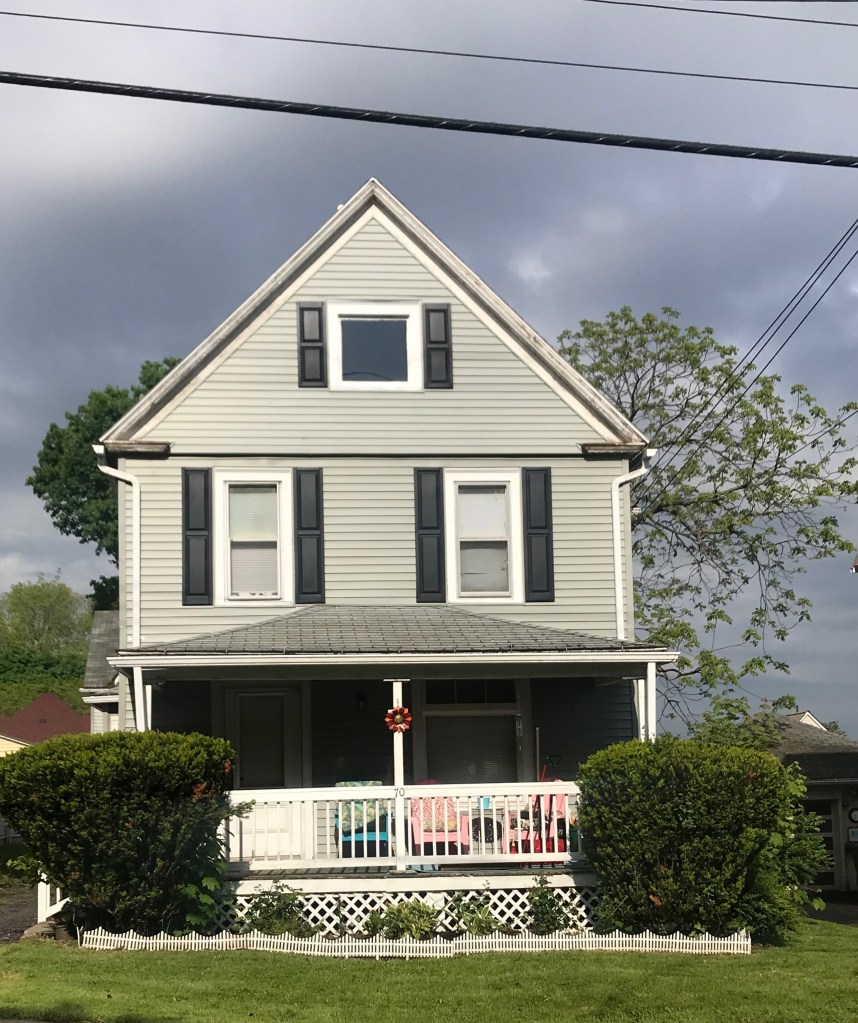 green house with black shutters and white porch and hedges