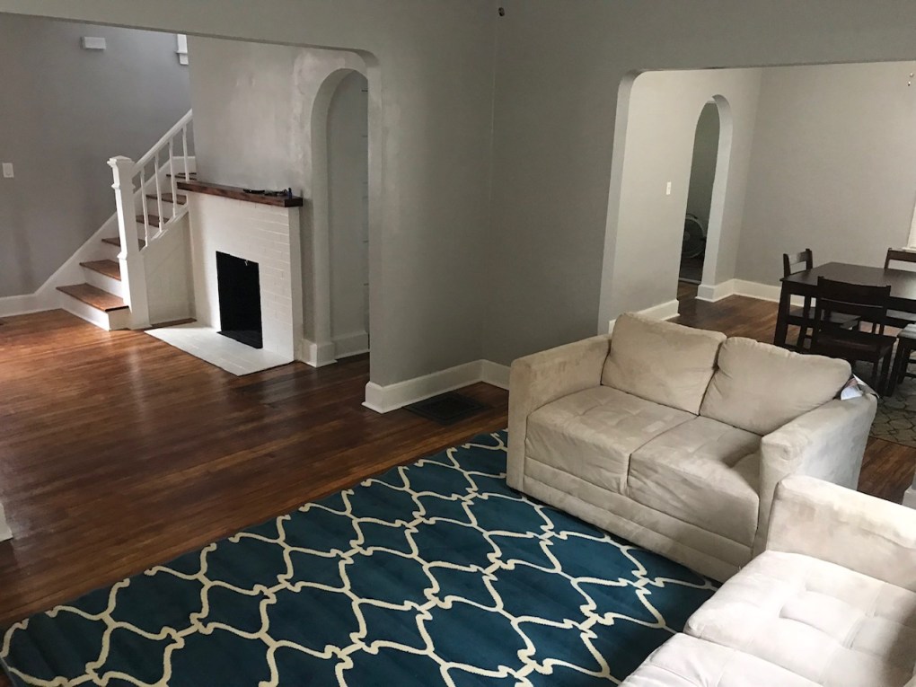 living room and dining room and entry way. wood floor and blue rug and white sofas. white fire place and stairs next to fire place