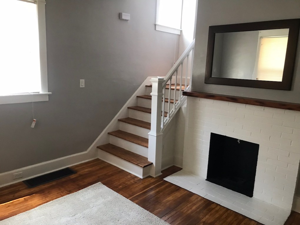 white fire place with mirror above and stairs next to fireplace