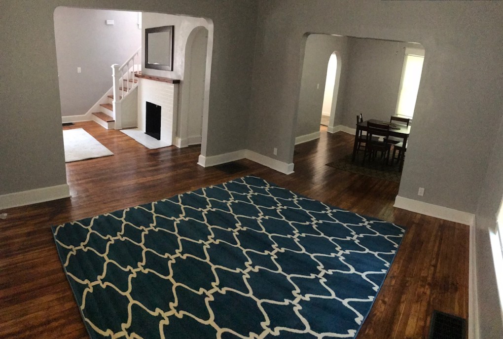 living room and dining room and entry way. wood floor and blue rug. white fire place and stairs next to fire place