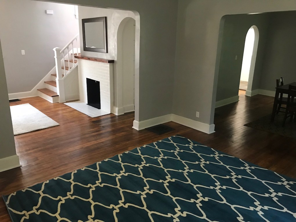 living room and dining room and entry way. wood floor and blue rug. white fire place and stairs next to fire place
