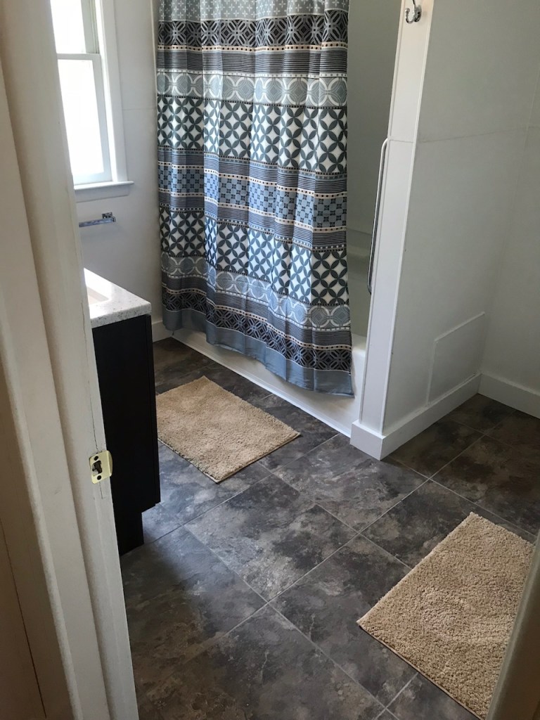 black tile floor with brown mats and blue shower curtain