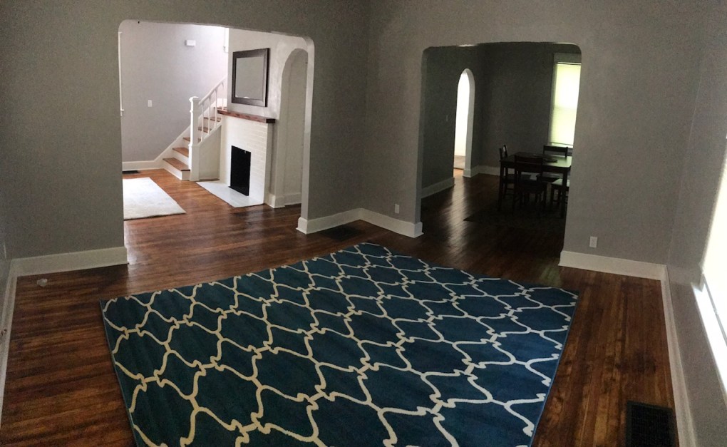 living room and dining room and entry way. wood floor and blue rug. white fire place and stairs next to fire place