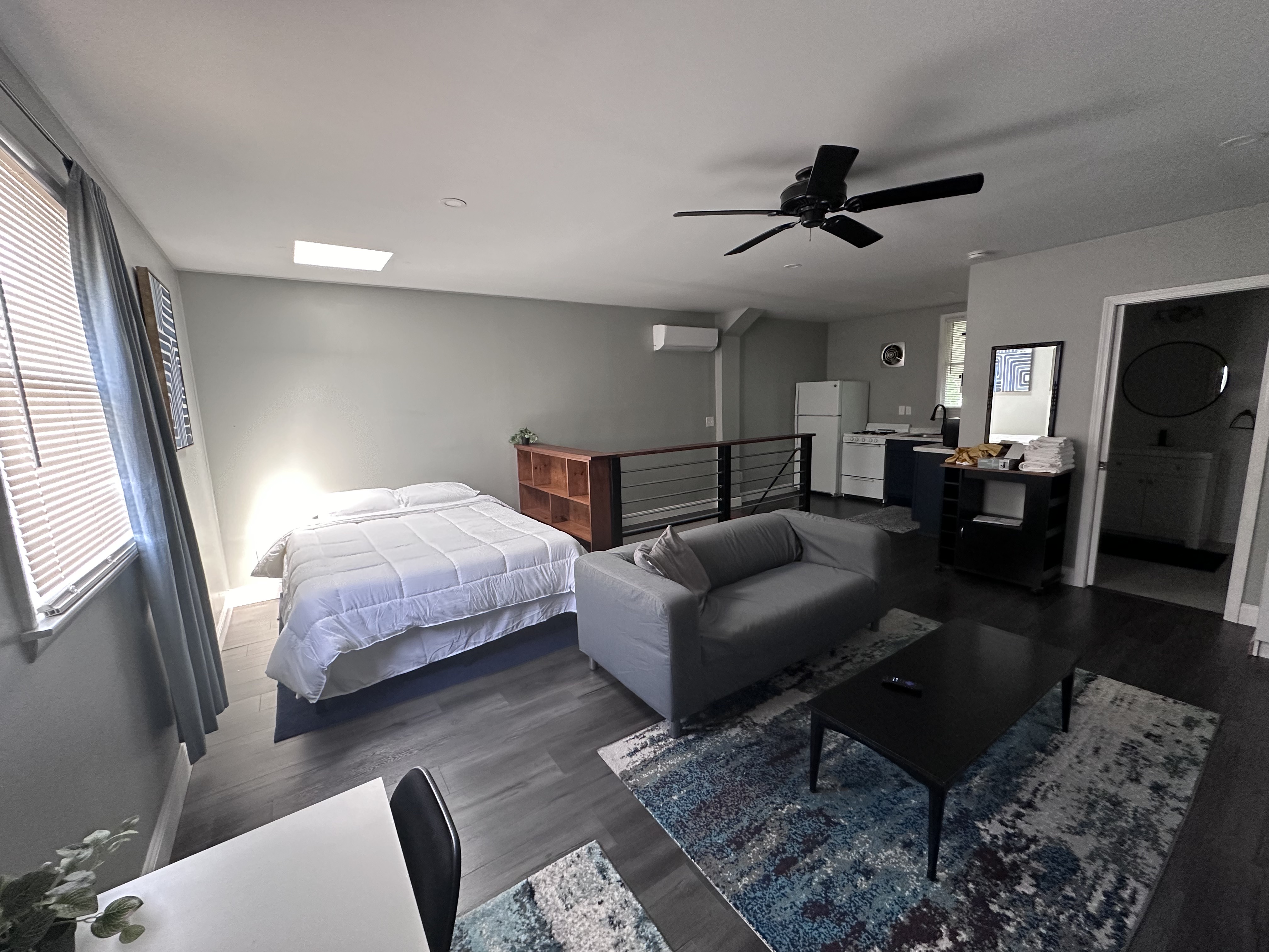 Picture of a studio apartment. White bed with gray couch and multicolored rug.